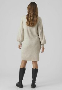 Robe pull en beige clair avec des manches longues bouffantes et une silhouette cintrée, associée à des bottes noires hautes pour le contraste.