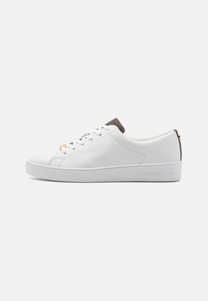 Baskets basses blanches avec lacets blancs, languette et contre-talons gris foncé, avec un nom de marque subtilement embossé sur le côté de la semelle.