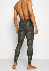 Dopasowane legginsy w kamuflaż w odcieniach zieleni, z czarną gumką w talii z logo, wykonane z elastycznego materiału dla komfortu.