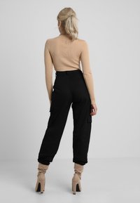 Pull côtelé beige à col montant ; pantalon cargo noir avec poches latérales ; bottines beiges à talons montant à la cheville.