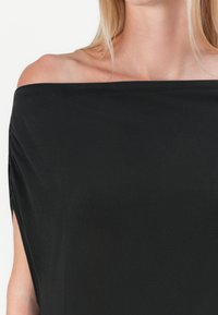 Zwarte off-the-shoulder top van zachte stof. Heeft een losse pasvorm met geplooide details aan de zijkanten en een elegante draping.