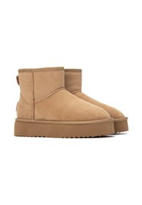 Botines de ante en tono beige con puntera redonda, suela plana de goma y tirador en el talón. Diseño sencillo con detalles de costura en la parte superior.