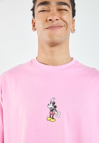 Rosa bomull t-skjorte med trykket grafikk av en tegneseriefigur, med rund hals og korte ermer.