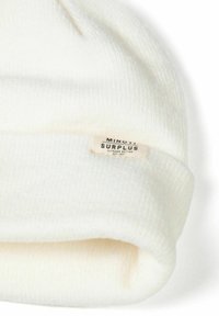 Bonnet en tricot blanc avec une texture côtelée et un revers replié. Comprend une petite étiquette de marque avec "Minoti Surplus" visible sur le côté.