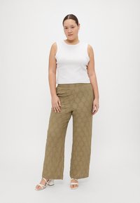 Λευκή χωρίς μανίκια μπλούζα με στρογγυλή λαιμόκοψη, συνδυασμένη με ελαιόχρωμο παντελόνι χαλαρής γραμμής που διαθέτει ανάγλυφο διακυμάνσεων σε διαμαντένιο σχέδιο.