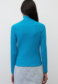 Turquoise geribbelde coltrui met lange mouwen, aansluitend model, zachte textuur en hoge kraag, gecombineerd met een gewatteerde grijze rok.