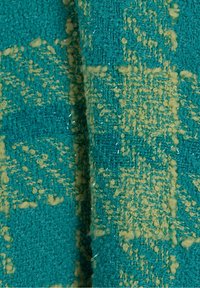 Gros plan d'un tissu tissé texturé bleu sarcelle et beige avec des motifs de fils bouclés et une surface légèrement rugueuse.