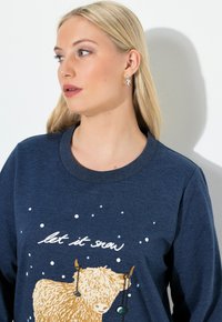 Granatowy sweter z teksturowaną ilustracją wysokogórskiego bydła, płatków śniegu oraz napisem "niech pada śnieg" w białym kolorze. Prosty dekolt okrągły.
