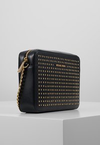 Borsa a tracolla rettangolare nera con borchie dorate, zip dorata e tracolla a catena, con marchio Michael Kors sul pannello frontale.
