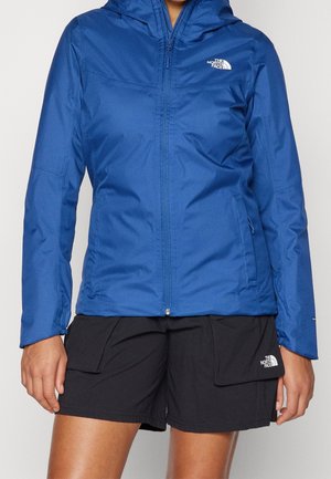 Person wearing a blue hooded North Face jacket zipped up and black North Face shorts with large front pockets.