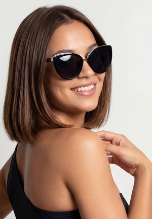 Kobieta z brązowymi włosami do ramion, uśmiechająca się, nosząca czarne okulary przeciwsłoneczne w kształcie kocich oczu i czarny bezrękawnik, patrząca przez ramię.