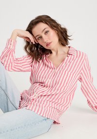 Chemise à rayures roses et blanches à manches longues avec col, poche et poignets à boutons, assortie à un jean en denim bleu clair.