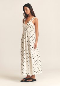 Maxiklänning i krämfärg med svarta prickar. Har v-ringning, rynkad överdel, breda axelband och en flödande kjol. Matchas med svarta flipflops.