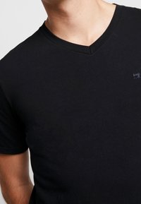 Sort V-hals T-shirt lavet af blødt bomuld. Har en diskret logo detail. Korte ærmer og et tætsiddende design.