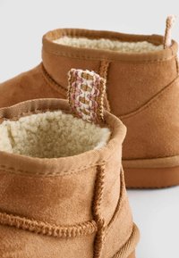 Barna nubukbőr bokacsizmák puha, krémszínű fleece béléssel. Figyelemre méltó, rózsaszín és természetes szálakból készült szőtt húzófül a hátoldalon.