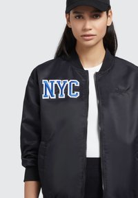 Mustmustarveti jakk musta värvi, millel on sinine ja valge "NYC" plekk. Omab luku eest, ribatud varrukaid ja sileda, läikiva kanga tekstuuri.
