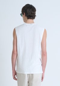 Top blanco sin mangas de tejido ligero con un acabado suave y texturizado. Cuello redondo, ajuste ligeramente holgado y aberturas laterales.