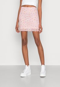 Mini-jupe rose avec des motifs de marguerites blanches, ourlet festonné, coupe ajustée, associée à des baskets montantes blanches et un top court blanc.