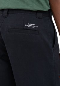 Schwarze Hose mit glatter Textur, ausgestattet mit einer Gesäßtasche und einem weißen, gestickten "Element Skateboard Co." Logo auf der rechten Seite.