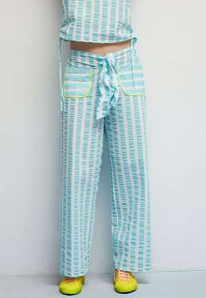 Jasnoniebieskie, szerokie spodnie w paski z dopasowaną talią, wyposażone w dwie przednie kieszenie obramowane żółtym pipingiem oraz teksturowaną tkaninę.