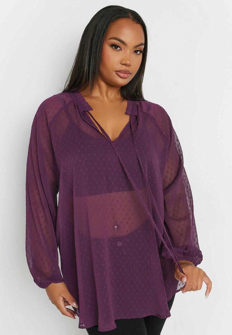 Blusa trasparente viola con motivo a pois, scollatura a V, dettaglio con fiocco e maniche a palloncino, dotata di polsini elasticizzati e vestibilità rilassata.