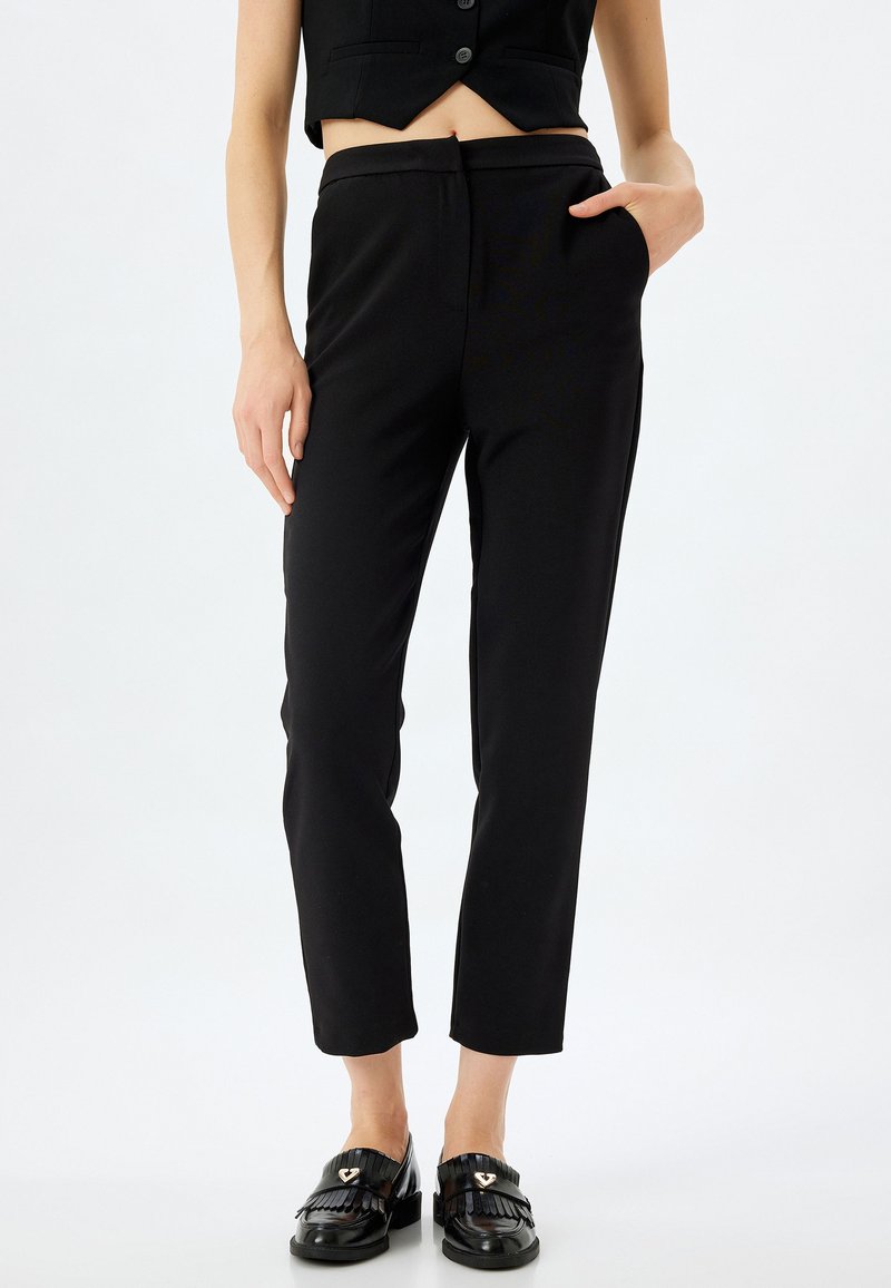 Pantalons noirs ajustés avec une coupe slim, dotés d'une texture lisse, de poches latérales et d'une taille plate, associés à des mocassins noirs.