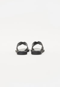 Sorte lær sandaler med flat såle, åpen tå-design og to kryssede stropper bak for støtte. Glatt tekstur.