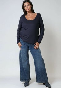 Donkerblauwe langarmpul met een ronde hals, gecombineerd met wijde blauwe jeans en puntige enkellaarsjes. Eenvoudig ontwerp met een textuurstof.