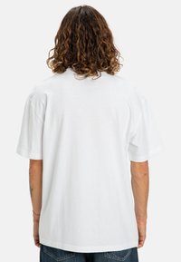 Camiseta de algodón blanca con corte relajado, mangas cortas y cuello redondo, con un respaldo liso y una textura suave.