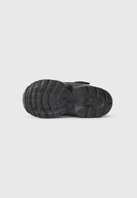 Sola de um tênis Nike preto com padrões de pisada detalhados e o logo da Nike no calcanhar, exibido contra um fundo branco.