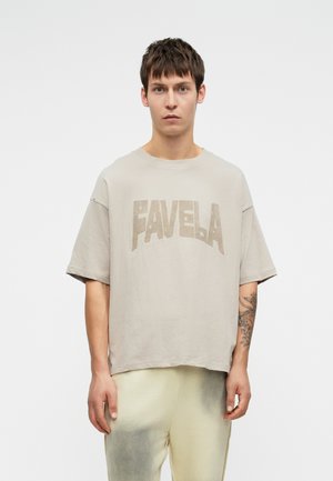 Beige graafiline t-särk, millel on sõna "FAVELA" paksude tähtedega. Omab mugavat lõiget ja lühikesi varrukaid, valmistatud pehmest, tekstuurist kangast.