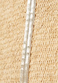 Tela de paja tejida en beige natural con una franja decorativa central de lentejuelas plateadas, creando un contraste texturizado contra el fondo.