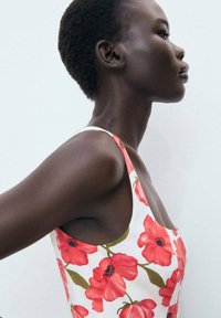 Floral dress featuring red poppy patterns on a white background, with a fitted design and thin straps. Smooth, lightweight fabric.
