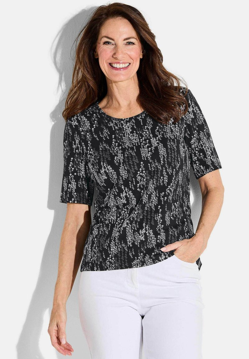 Haut noir à manches courtes avec un motif abstrait texturé blanc. Encolure ronde et coupe décontractée. Assorti avec un pantalon blanc.