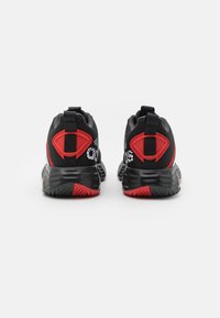 Baskets de sport noires et rouges avec une tige en mesh, un talon texturé et un motif de semelle distinct ; accents réfléchissants sur les côtés.