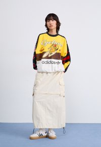 Sudadera de mangas largas y colores vibrantes con estampado gráfico en amarillo, negro y rojo. Combinada con una falda estilo cargo beige y zapatillas blancas.