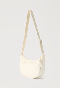 Κρεμ χρωματισμένη τσάντα ώμου σε σχήμα ημισελήνου με ρυθμιζόμενο ιμάντα και μικρή μπροστινή τσέπη με φερμουάρ σε μονόχρωμο φόντο.