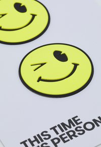 Dois autocolantes de caras sorridentes amarelas com contornos e características faciais pretas, posicionados sobre um fundo branco com texto preto abaixo.