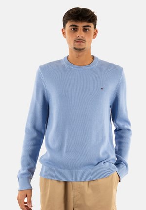 Maglione azzurro chiaro lavorato a maglia con collo rotondo, polsini e bordo a coste, caratterizzato da un piccolo logo sul lato sinistro del petto. Texture liscia.