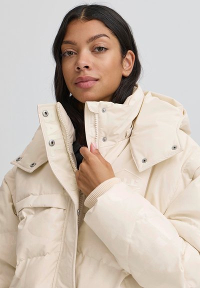 Gaismas bēša puffer jaka ar augstu apkakli, metāla spiedpogu aizdari un ribotu aproču maliņu. Vienmērīga tekstūra ar smalku logotipa detaļu.