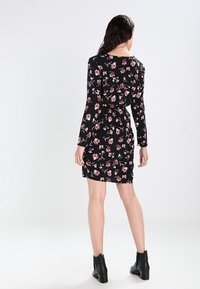 Černé květinové šaty s dlouhými rukávy, které mají přiléhavý střih a stahovací pás. Tkanina má jemnou texturu a pestrý květinový vzor.