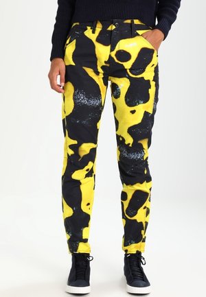 Jeans ajustados con un audaz patrón amarillo y negro que presenta formas abstractas. Hechos de mezclilla con una textura suave. Cuenta con el clásico diseño de cinco bolsillos.