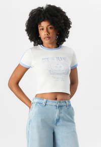 Valge lühikeste varrukate ja sinise kaeluse ning varrukate servadega lühikeste varrukatega T-särk. Omab helesinist graafilist kujundust "GUESS JEANS" ja loorberikujundit. Heledad teksashortsid.