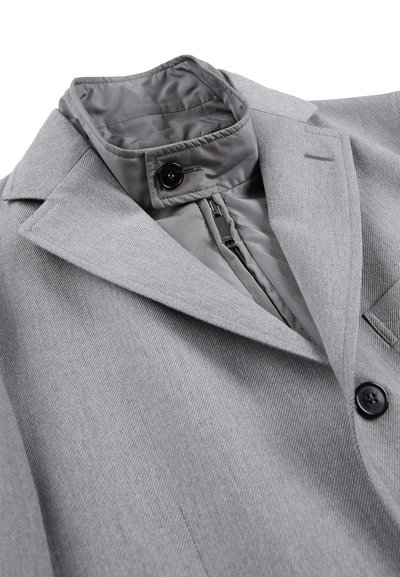 Blazer grigio su misura in tessuto testurizzato, con revers a becco e due bottoni neri. Presenta una sottile fodera interna a contrasto.