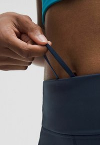 Námornícke legíny s vysokým pásom, hladkým povrchom a elastickým pásom. Ruka ťahá látkový popruh v páse pre úpravu.