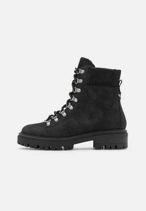 Schwarze Wildleder-Stiefelette mit dicker Sohle, geripptem gepolstertem Kragen, Metallösen und schwarzen Schnürsenkeln, seitlich dargestellt.