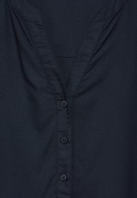 Camicia blu navy con scollatura a V, chiusura frontale con bottoni e tessuto morbido e testurizzato. Presenta cuciture lisce e cinque bottoni neri.