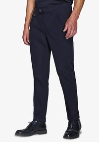 Chinos blu navy in cotone con una vestibilità slim, dotati di chiusura con bottone, tasche laterali e orli in fondo. Indossati con scarpe nere lucide.