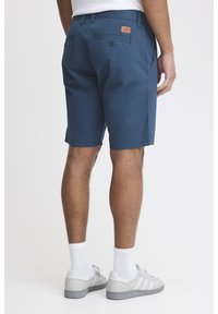 Blue shorts made of lightweight fabric with a smooth texture, featuring two back pockets and a leather logo patch on the waistband.
