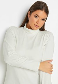 Vit långärmad turtleneck-tröja med en mjuk textur, med hög krage och åtsittande ärmar. Enkel, ren design utan mönster eller dekorationer.